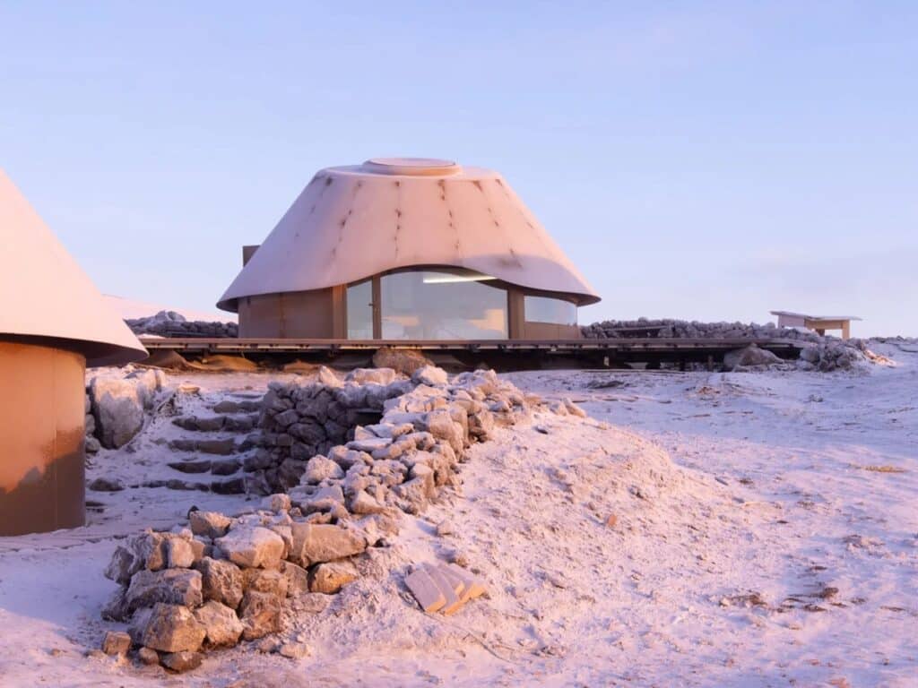 Low-angle shot of a cabin raised on a platform with a stone-paved path in a snowy environment.