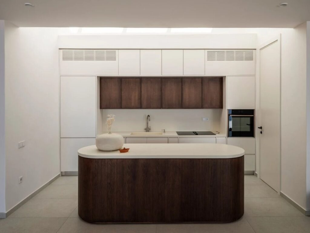 Modern minimalist kitchen with white cabinetry and a dark wood island under a skylight.