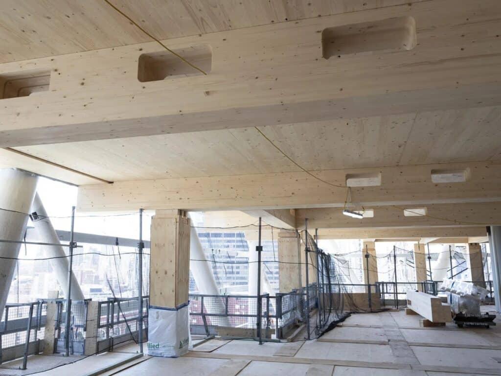 Wide interior shot of a floor under construction with exposed mass timber ceilings and temporary safety scaffolding.