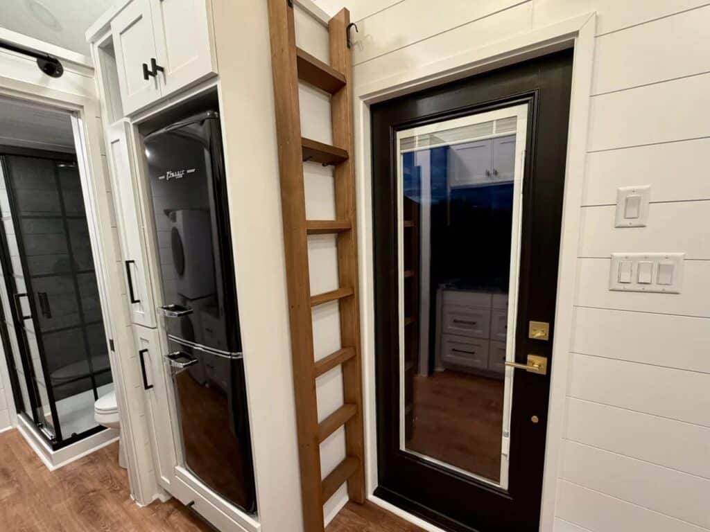 Close-up of the integrated appliances and a wooden ladder next to the glass entrance door in the Betty tiny house.