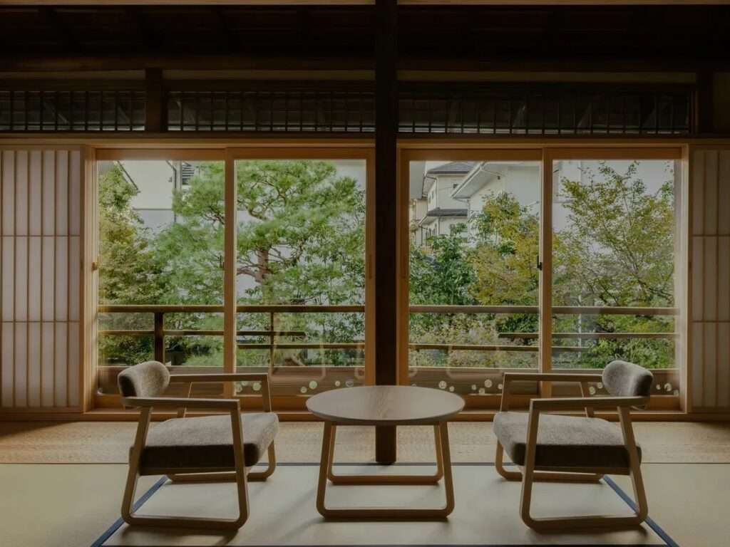Symmetric view of two modern chairs facing a wooden table in front of large sliding glass doors overlooking a garden.