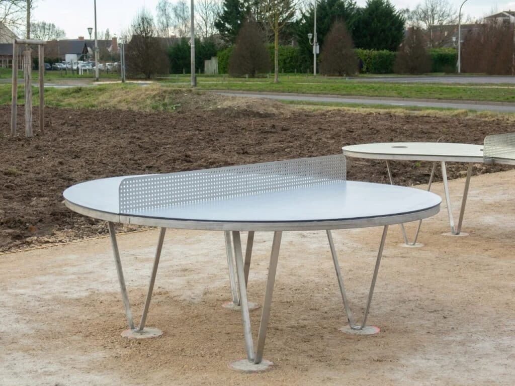A circular ping-pong table with a perforated metal net, highlighting durable industrial materials like galvanized steel.