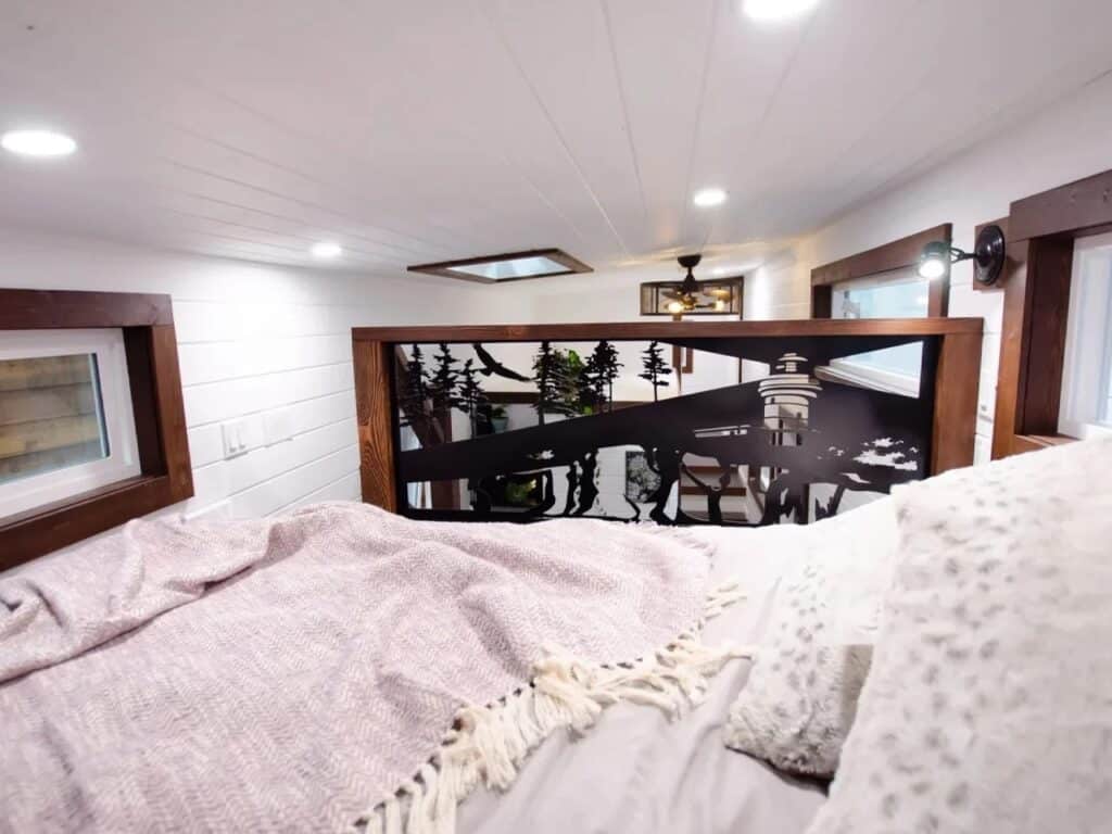 Tiny house loft bedroom with a decorative laser-cut metal railing featuring a forest silhouette.