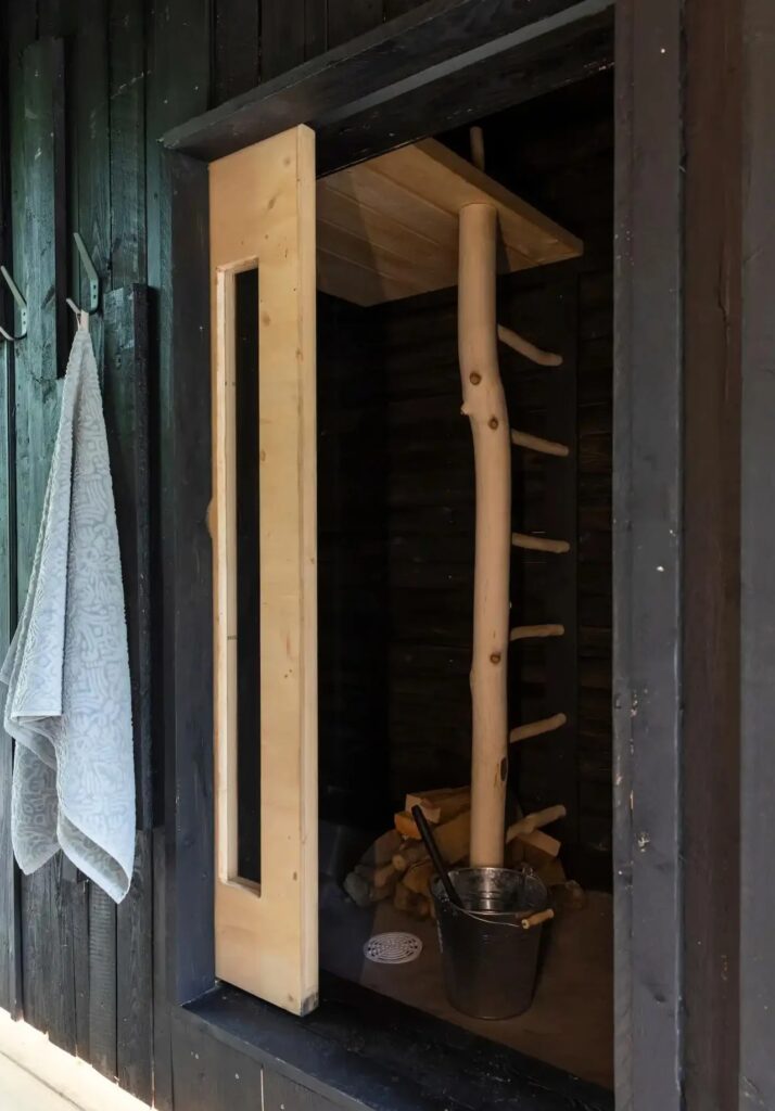 Small wood-fired sauna inside Tiny House Shadow featuring natural wood and rustic ladder.