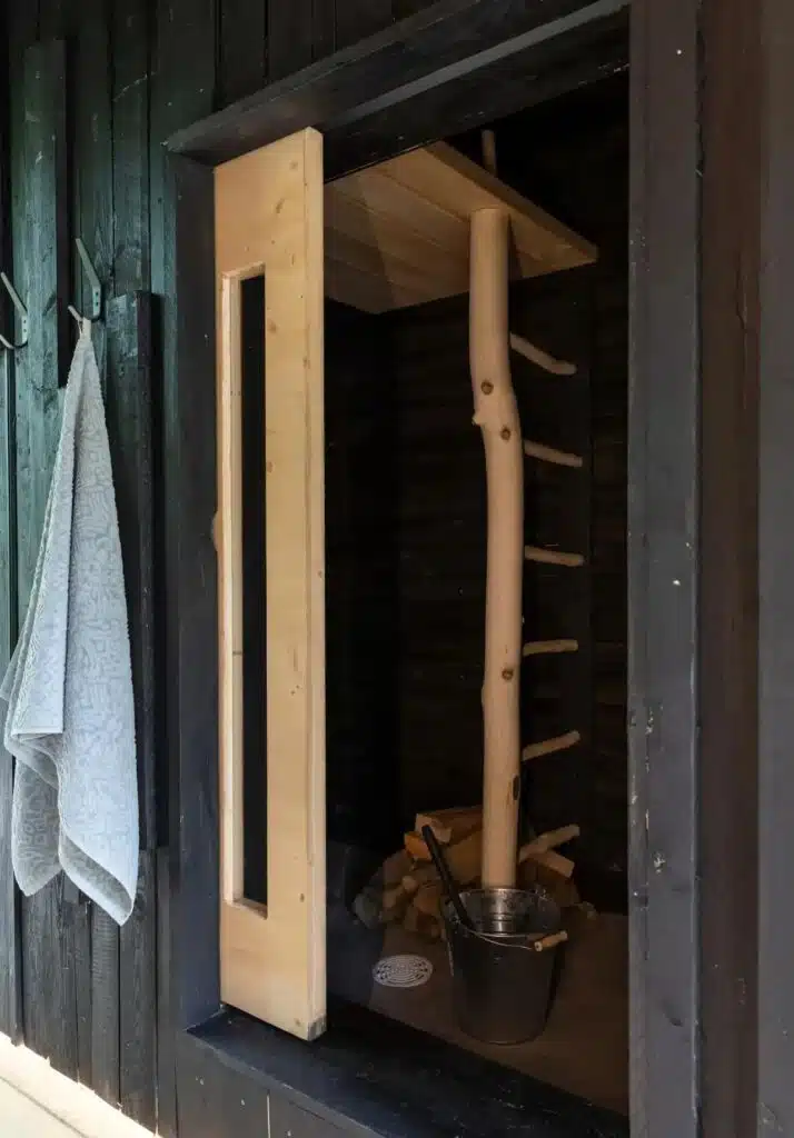 Small wood-fired sauna inside Tiny House Shadow featuring natural wood and rustic ladder.