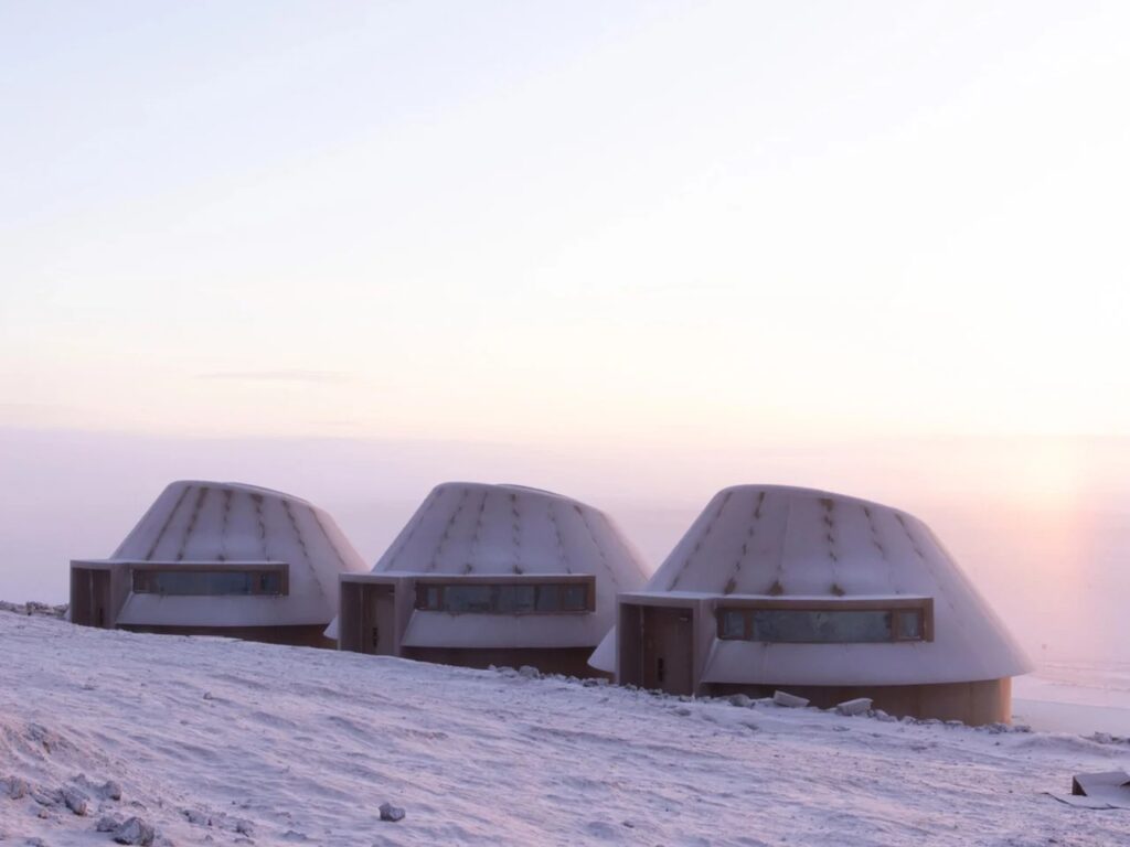Side view of three identical architectural cabins showing horizontal windows and curved protective walls.