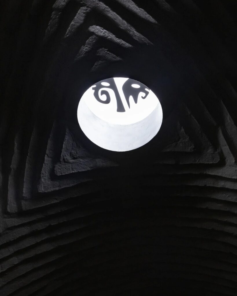 Close-up of a circular skylight (oculus) at the apex of an adobe brick vault with a decorative metal grate.