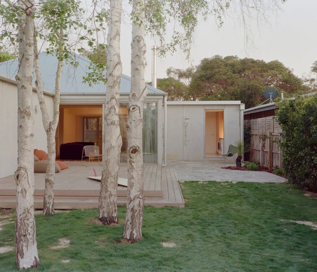 Outdoor courtyard with stone paving, a wooden deck, birch trees, and an outdoor shower area.
