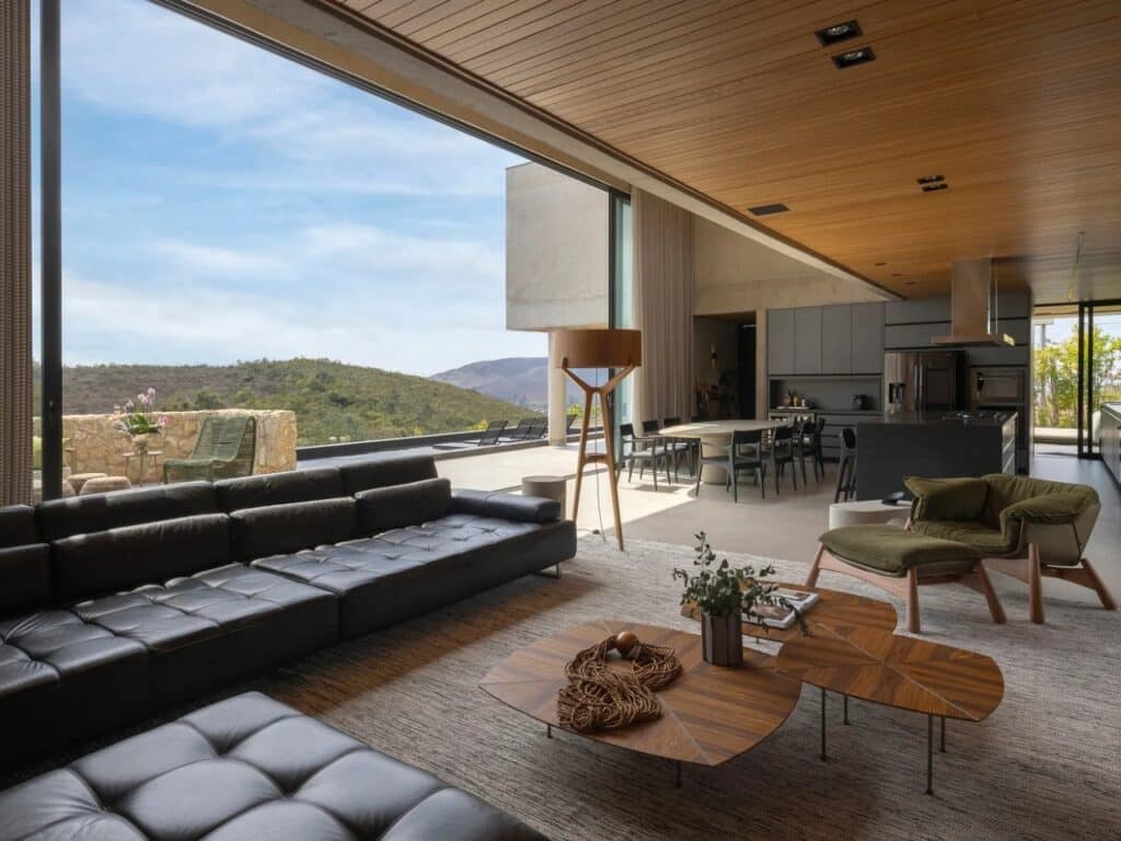 Interior of GM House living room with black leather sofa and panoramic glass window overlooking a valley.