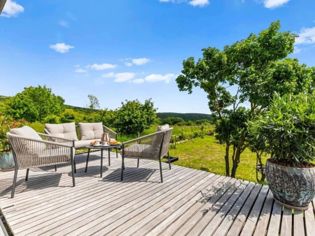 Wide angle of the Devin Cabin terrace featuring modern grey armchairs, a coffee table, and lush green surroundings.