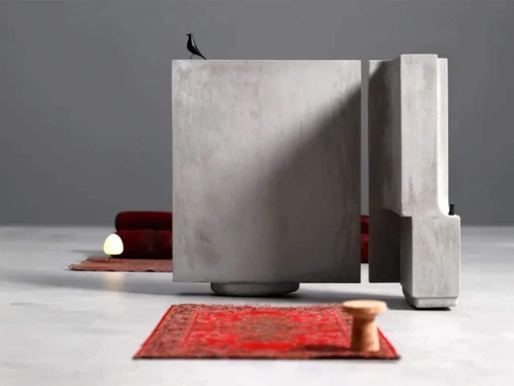 A minimalist composition of a concrete slab, a red rug, and a small bird figurine.