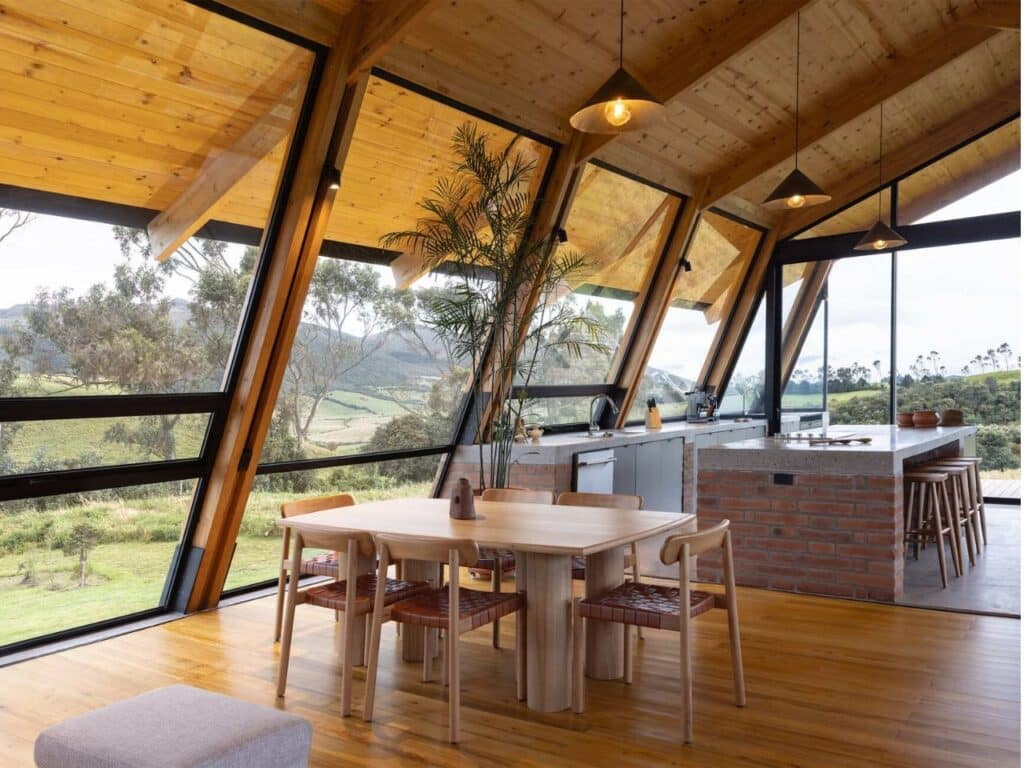 Modern kitchen and dining area in La Miradora with a brick island, wooden table, and expansive glass walls facing the valley.