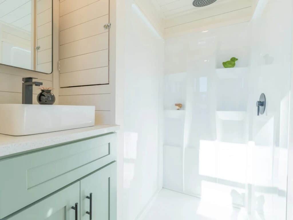 Minimalist tiny house bathroom with a white vessel sink, sage green vanity, and a bright walk-in shower.