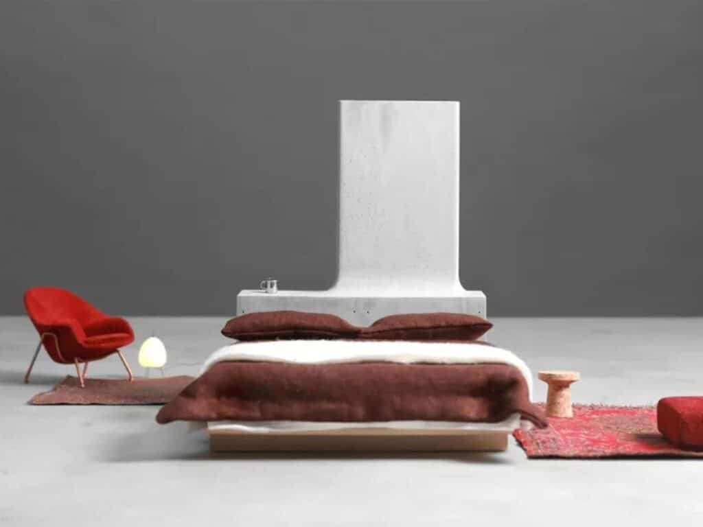 A double bed positioned in front of a large L-shaped concrete headboard in a minimalist room.