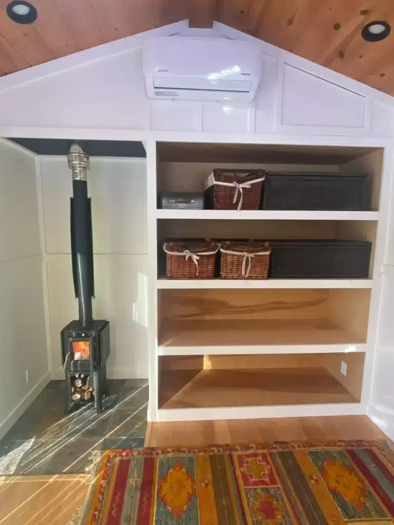 Built-in wooden shelving and a small black wood-burning stove on a tiled floor inside the mobile unit.