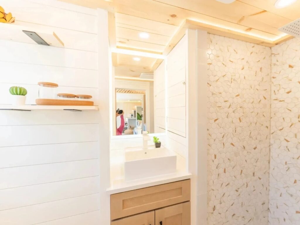 Modern bathroom in a tiny house with hexagonal tiled shower walls and a fog-free LED mirror.