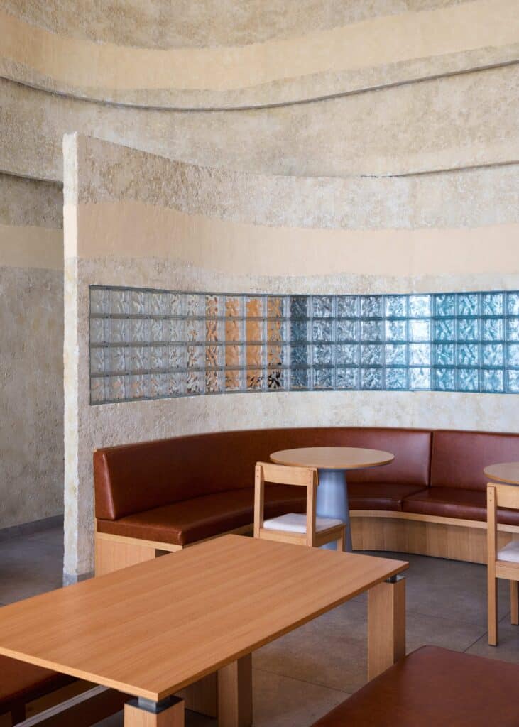 Curved interior wall with layered plaster finish and blue glass bricks behind a leather booth seating.