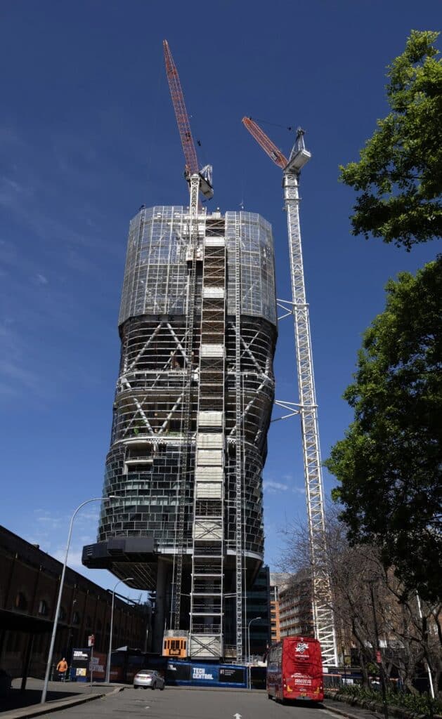 Full vertical shot of the Atlassian Central tower construction with cranes against a clear blue sky.