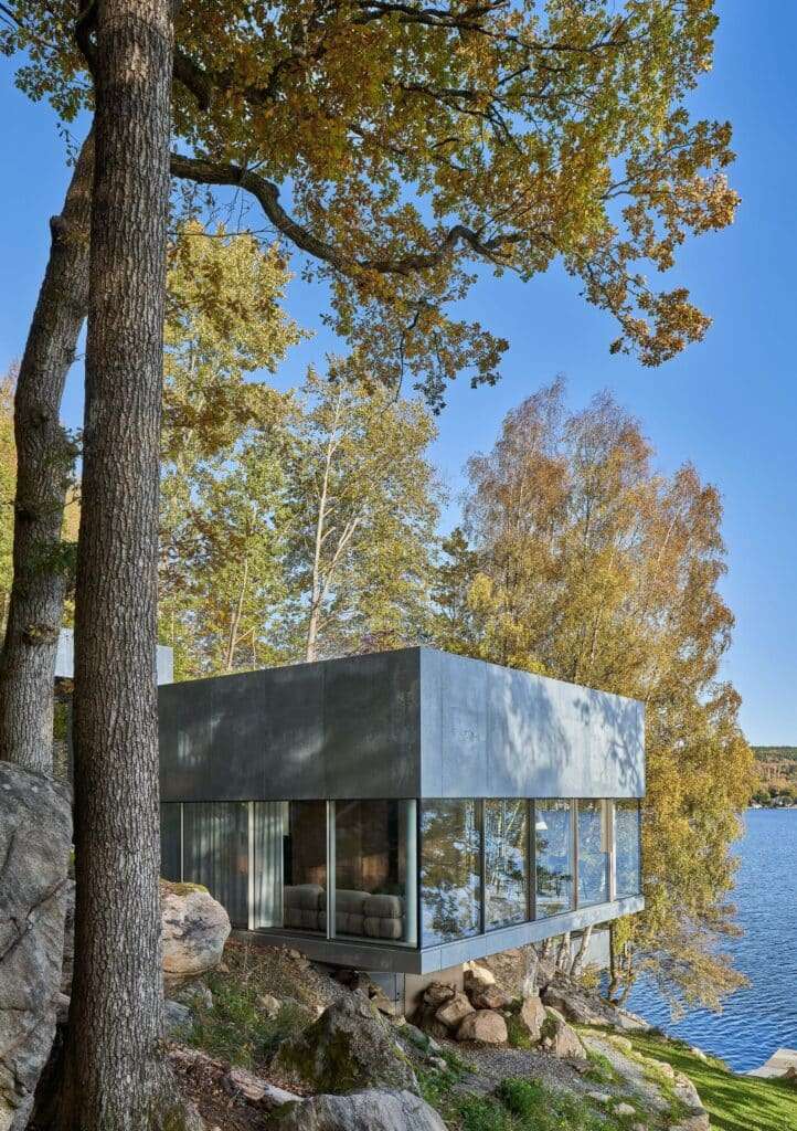 Side view of the Bor&aring;s Getaway House cantilevered over a rocky slope with autumn trees and a view of the lake.