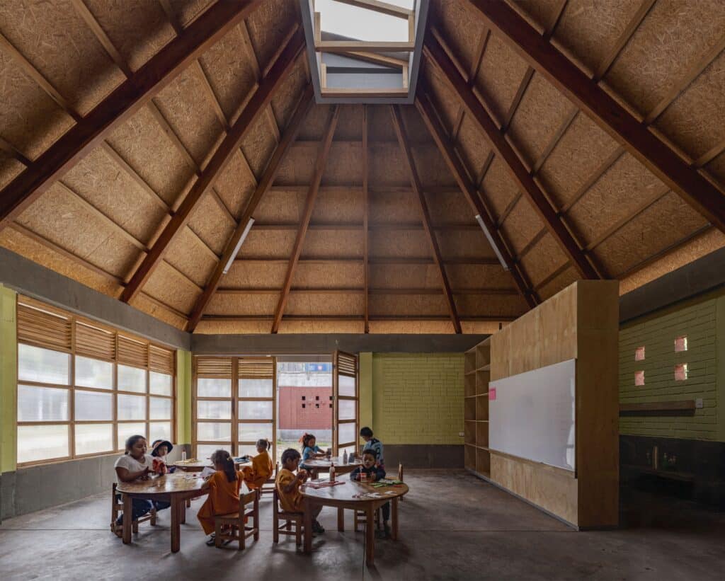 Interior of a classroom at Sonomoro School featuring a high pyramid wooden ceiling with a central skylight and children at round tables.