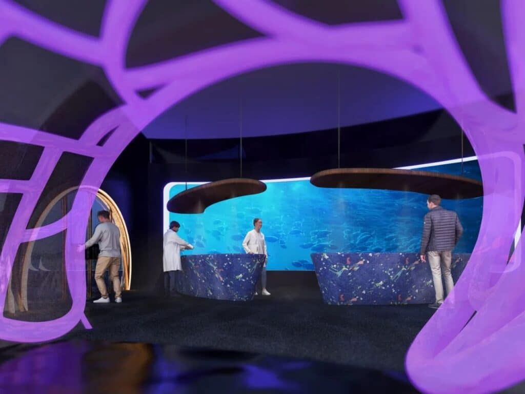 Reception desks with textured blue finishes and curved overhead lights in a space with a large aquatic screen.