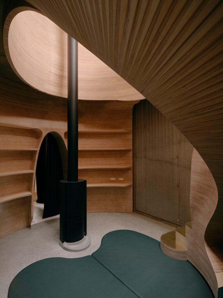 Interior of the circular snug room with plywood shelving, a black fireplace, and integrated green seating.