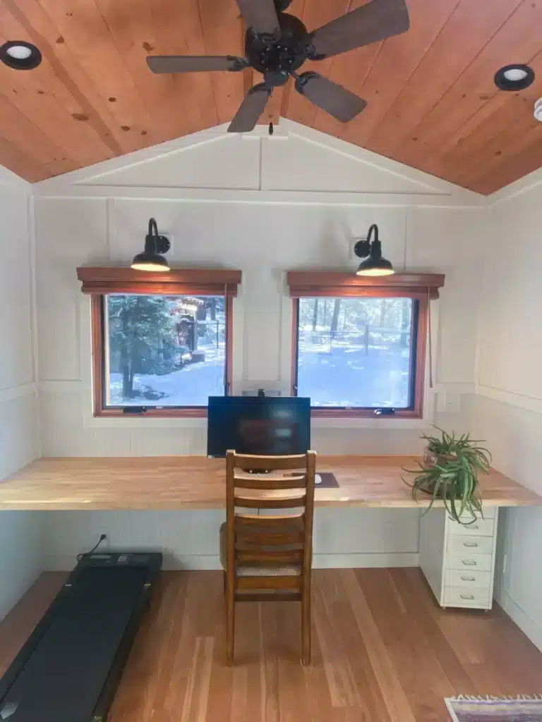 Modern workstation inside the mobile office with a large monitor, wooden desk, and a treadmill for active working.