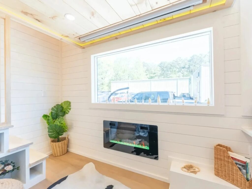 Living room detail showing an electric fireplace built into a shiplap wall under a large window.