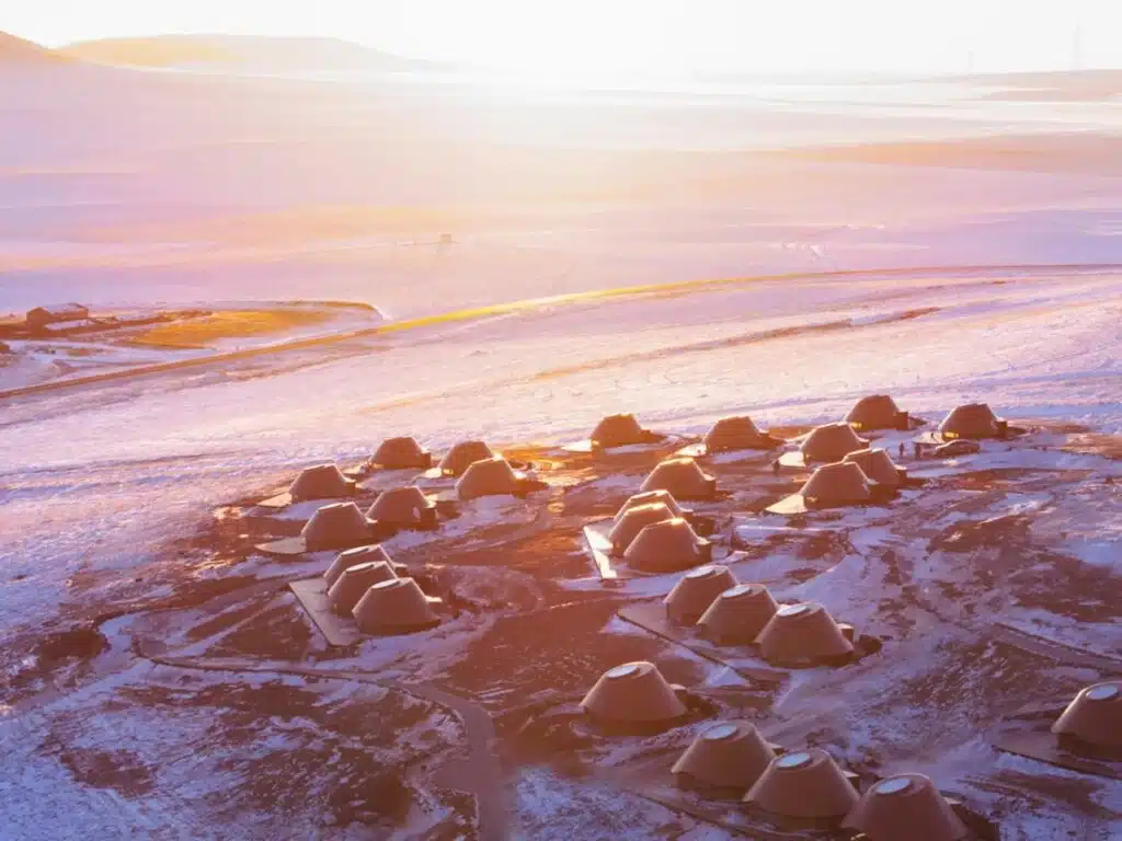 Golden hour aerial view of the Volcano-In resort with sunlight reflecting off the snow and cabin roofs.