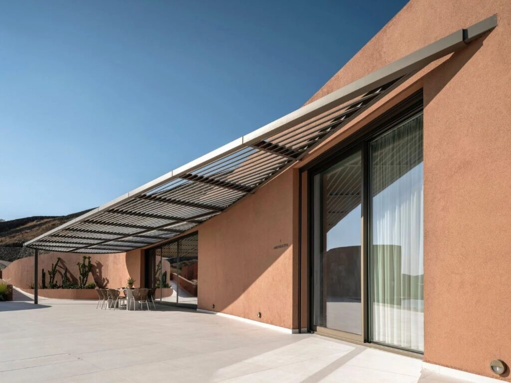 Architectural detail of Oline resort's earth-toned facade under a metal slat pergola with large sliding glass doors.