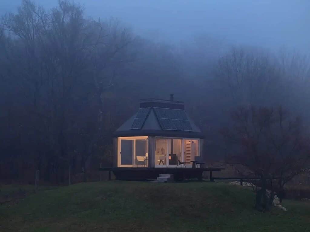 Devin Cabin glowing from within at night, surrounded by misty trees and a foggy atmosphere on a hill.
