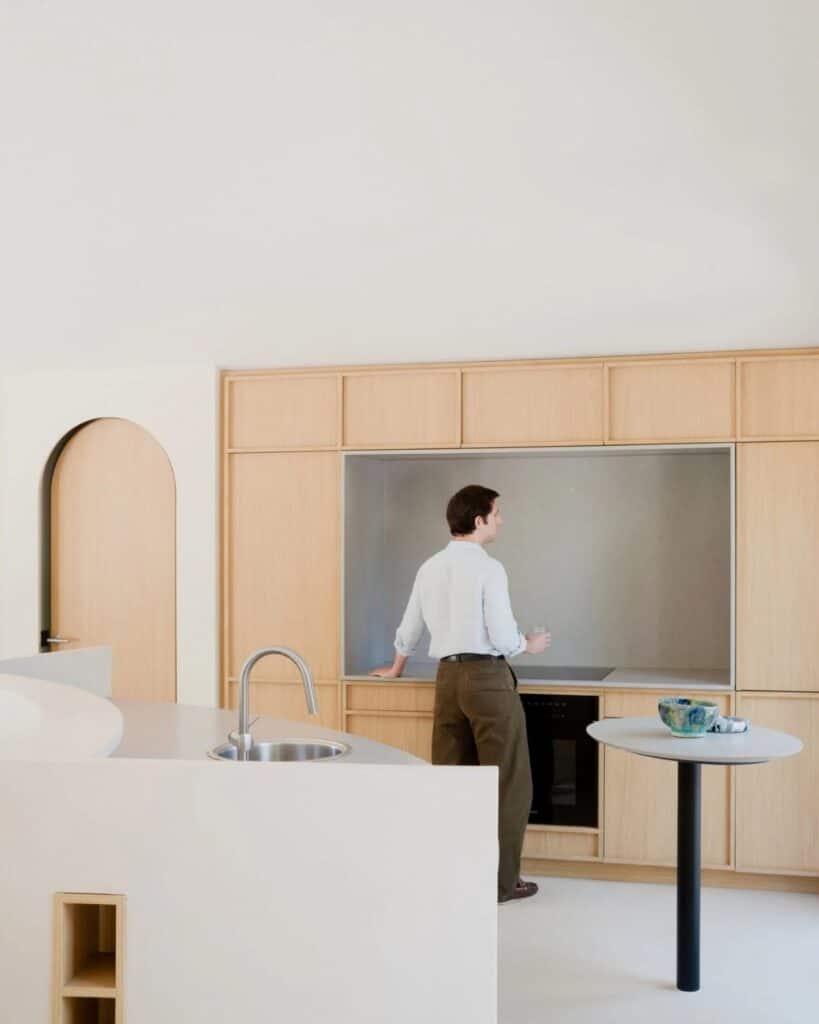 Modern minimalist kitchen in Seaside House with light wood cabinetry and a person standing at the counter.