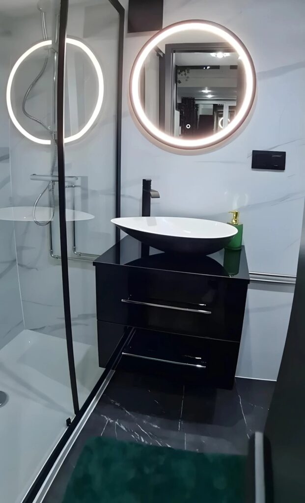 Modern bathroom in Erica tiny house with backlit circular mirror and black vanity.