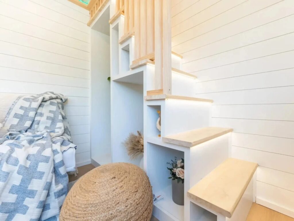 Close-up of integrated storage stairs in the Premium Vista tiny house featuring light wood treads and built-in white shelving cubbies.