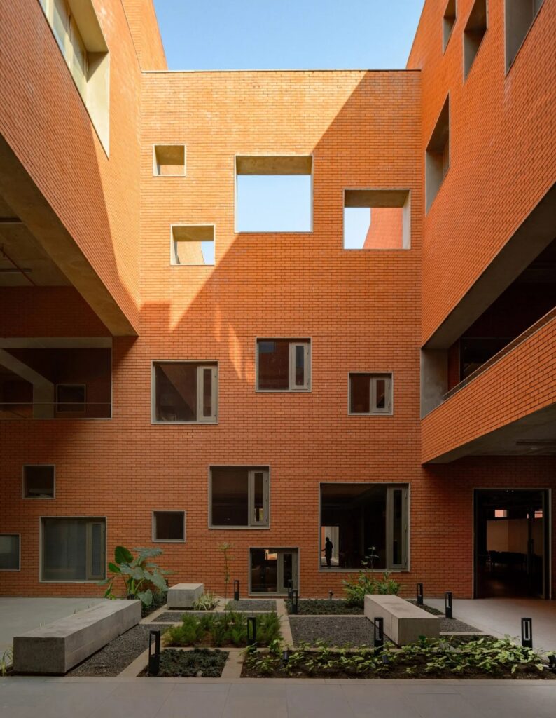 Internal courtyard with stone benches and irregularly placed windows in a brick wall.