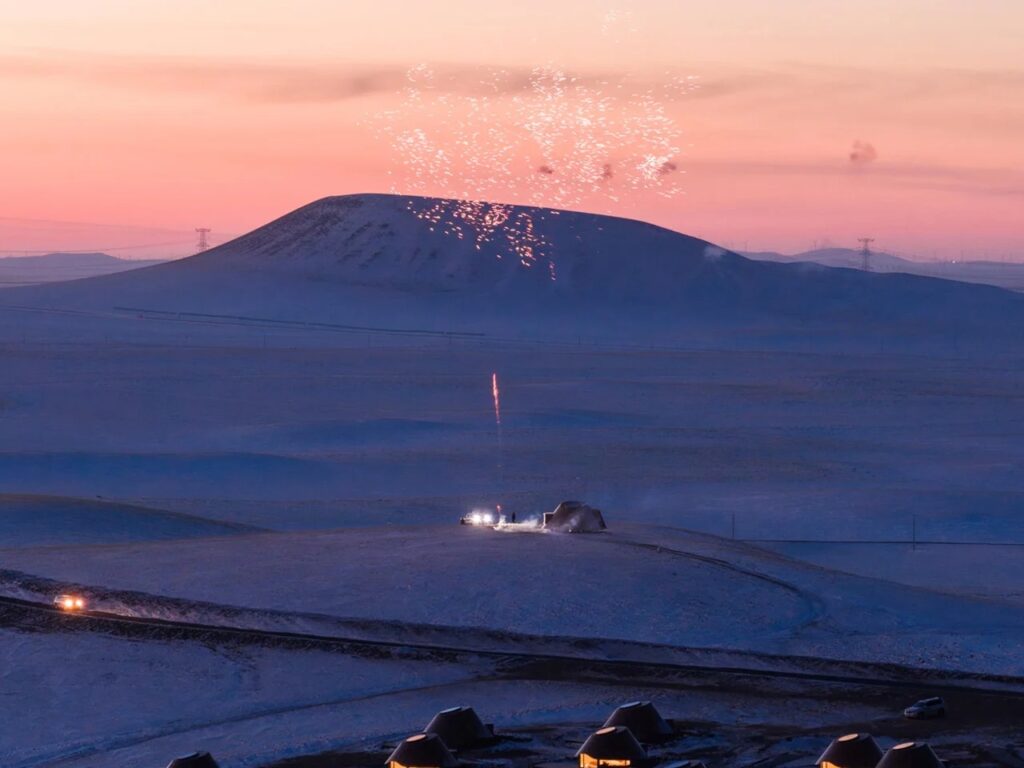 Night view of a volcano with lights/fireworks and the silhouettes of the architectural project in the foreground.