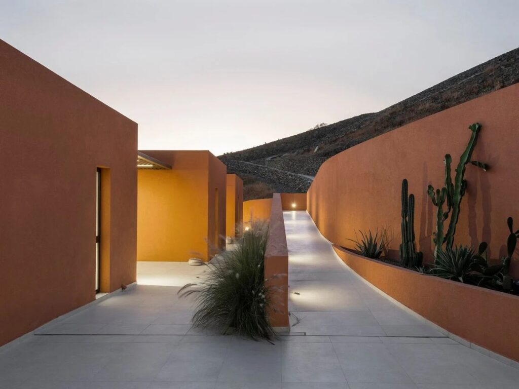 Evening view of the illuminated winding path and curved walls at Oline resort, leading between subterranean units.