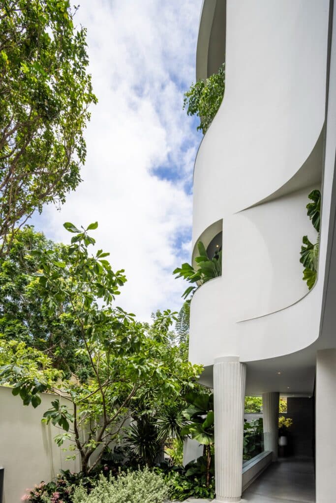 White fluted column supporting a curved upper floor next to a garden walkway.
