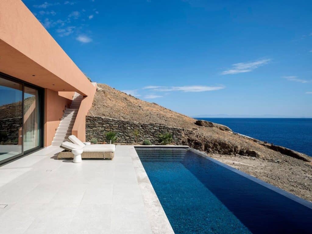 Outdoor terrace with a white stone floor, an infinity pool, and a minimalist sunbed overlooking the Mediterranean sea.