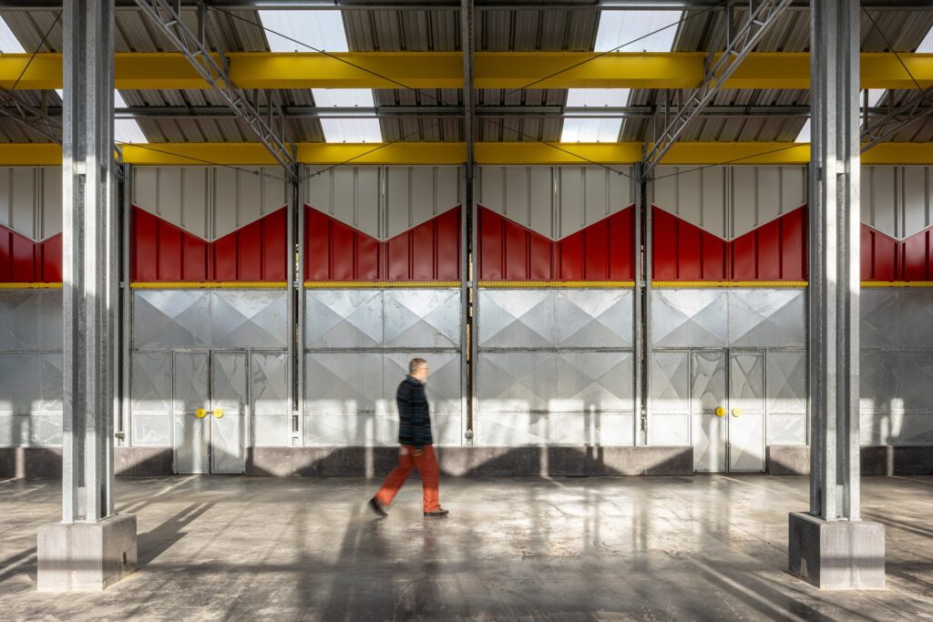 Symmetrical interior view of the barn structure highlighting the steel trusses and red sawtooth wall sections.