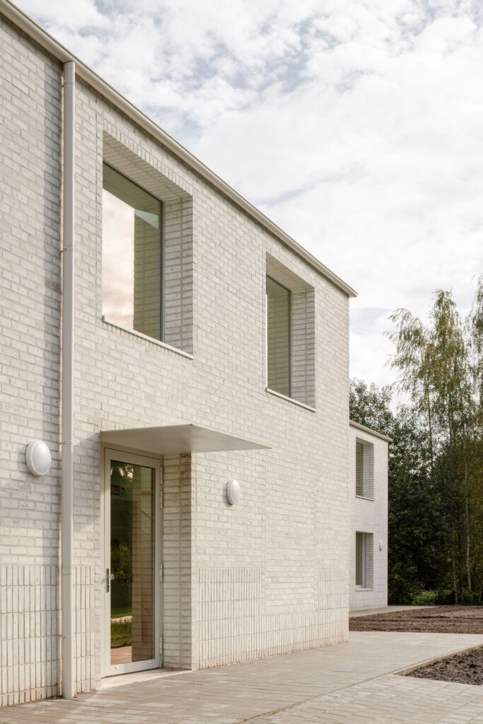 Minimalist entrance of Care Villa with a thin metal canopy, glass door, and vertical brick patterns on the lower part of the facade.