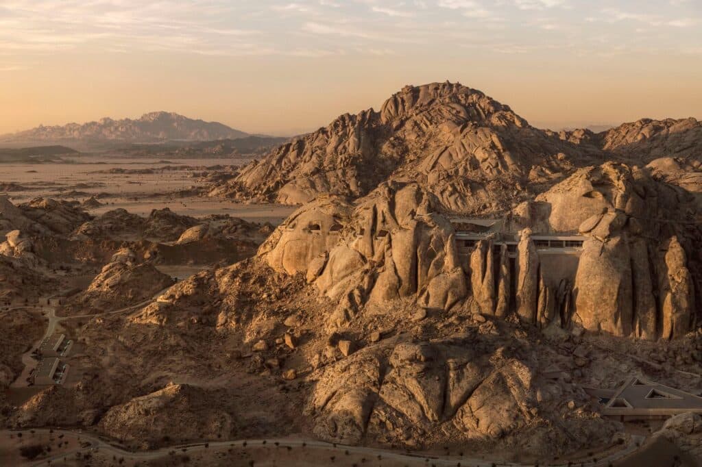 Aerial panoramic view of Desert Rock resort in the Saudi Arabian desert, showing structures camouflaged within the mountainous landscape.
