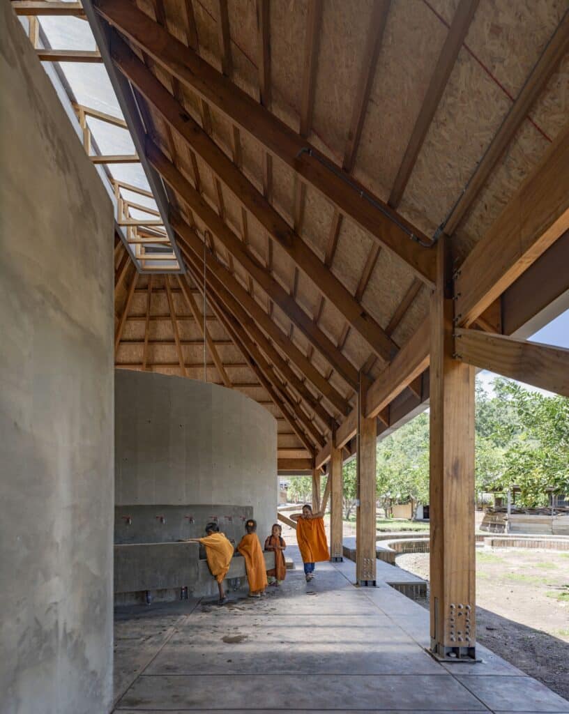 Children at an outdoor concrete wash station under the large eaves of the wooden roof at Sonomoro School.