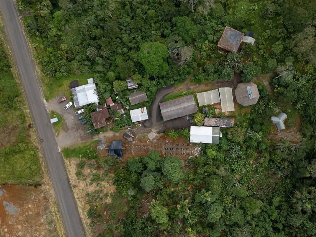 Wide aerial landscape view showing the Witocha Lab site, local road, and various community buildings nestled within the Amazonian forest.