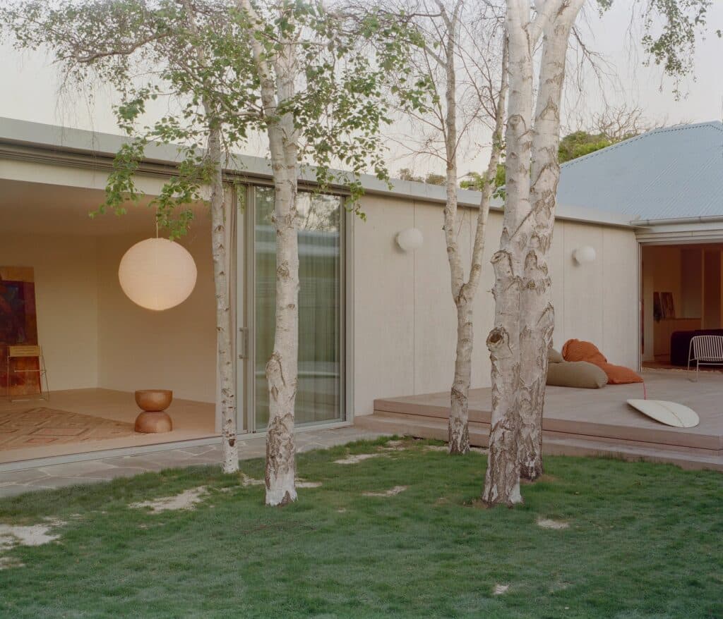 View from the lawn looking towards the timber deck and open living spaces under the shade of birch trees.