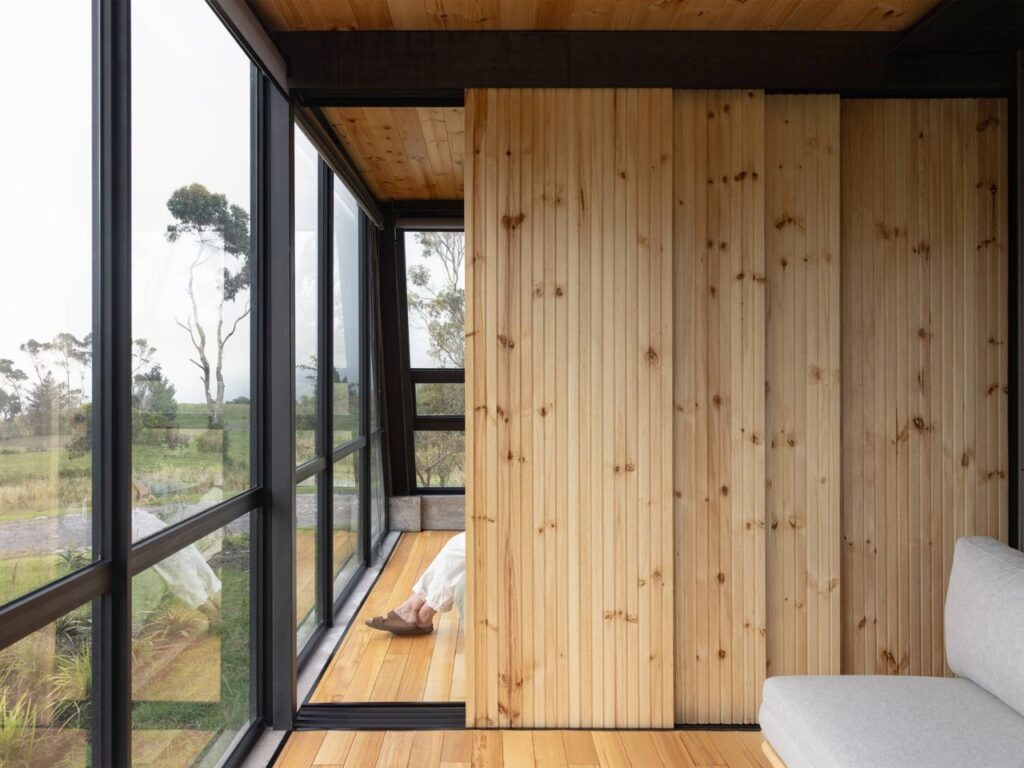 Close-up of vertical timber slat sliding doors in La Miradora, revealing a glimpse of a person and the exterior landscape through glass.