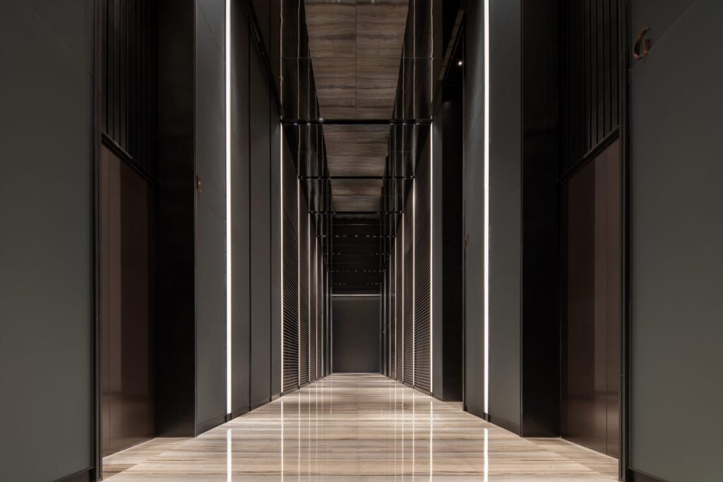 A symmetrical view of a modern elevator corridor in Jinan Tower with vertical stone panels and warm linear lighting along the floor and ceiling.