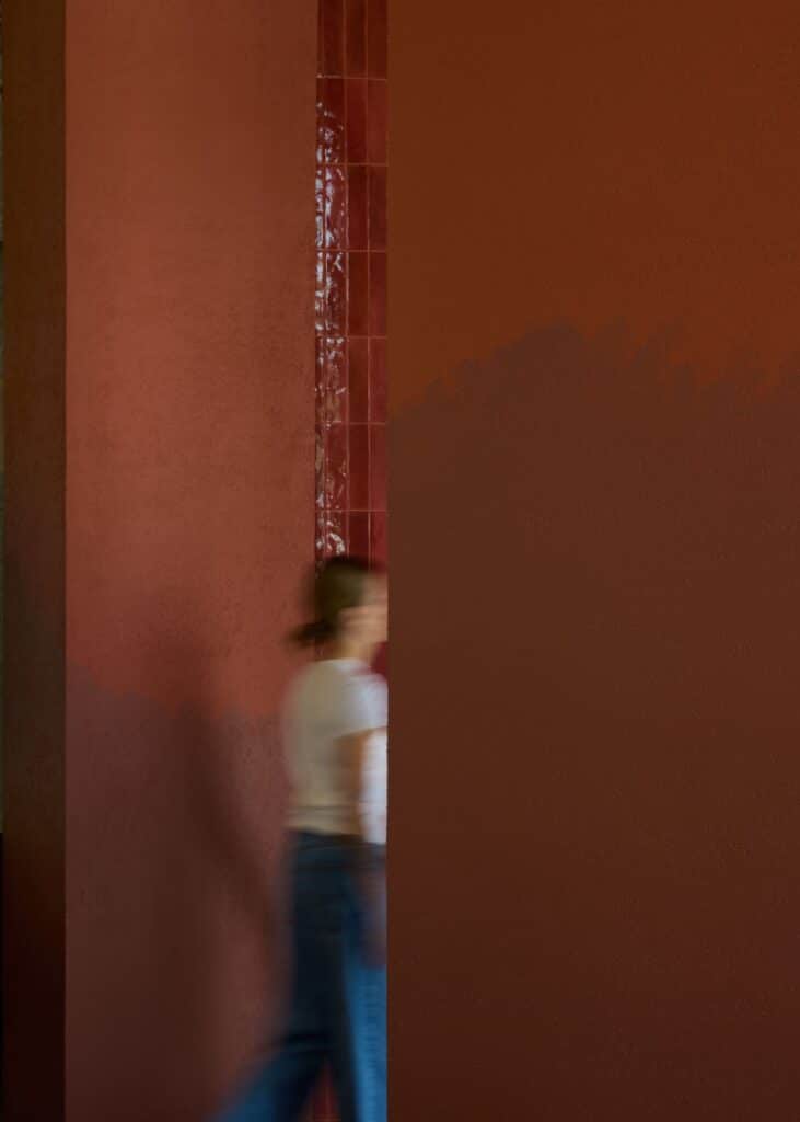 Close-up of a deep terracotta-colored architectural column with a glossy tile detail and a blurred person walking by.
