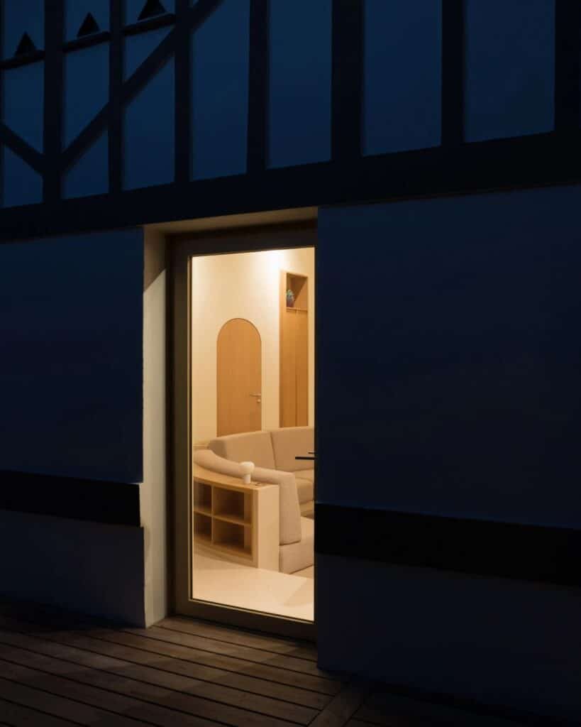 Night view through a glass door showing the warm minimalist interior of Seaside House and its curved furniture.