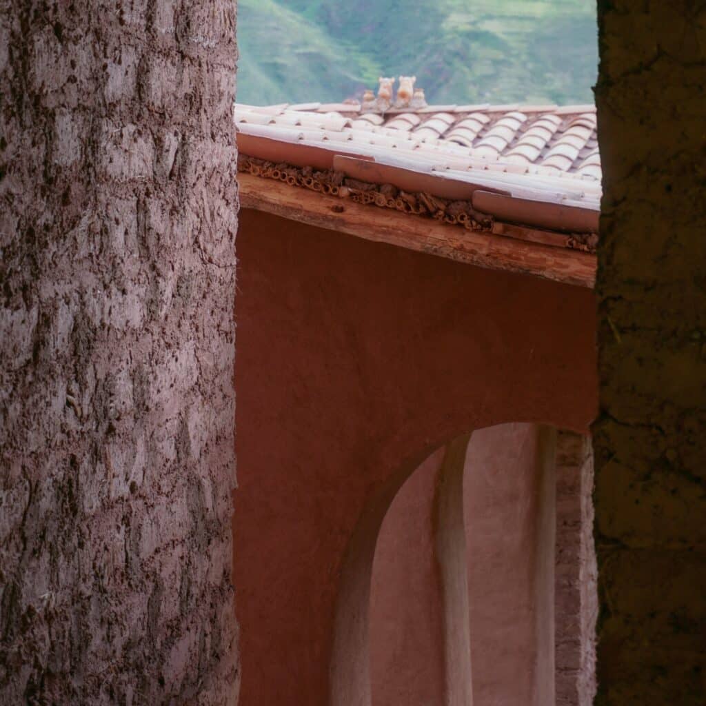 Close-up of textured adobe wall corner and clay roof tiles with mountain peaks in the background.
